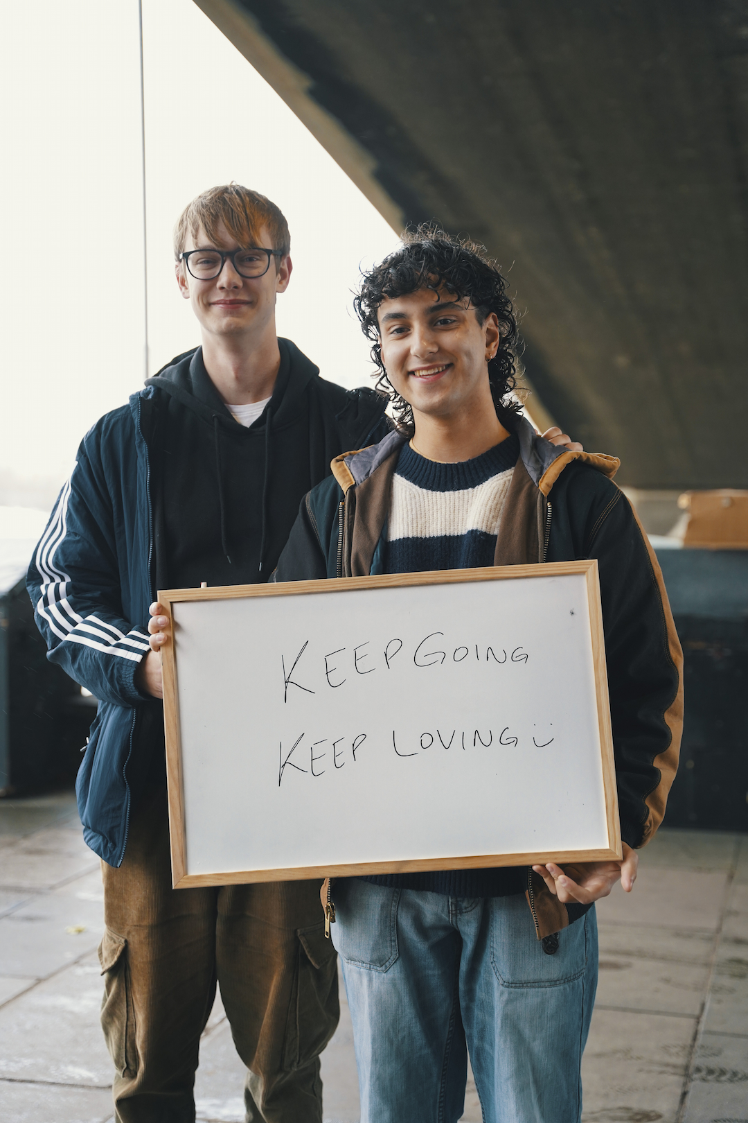 Two young adults holding a whiteboard saying 'Keep going, keep loving'.